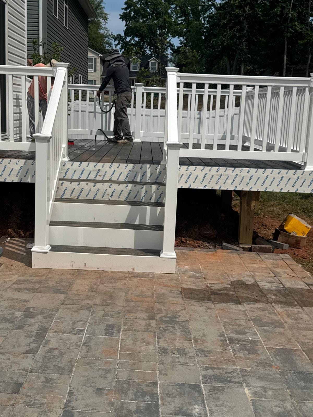 Deck with white railings and stairs over a new paver patio