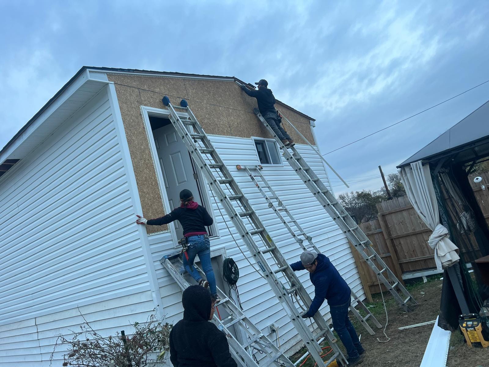 Crew on ladders installing siding on a house